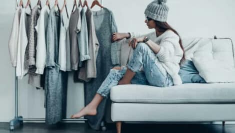 Young woman sitting on a couch and looking at clothes on a rack.